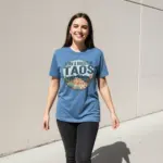 born-and-raised-in-taos-shirt-575-nm-city-pride-tee-comfort-colors-t-shirt-sunlight-female-blue-jean.webp Woman wearing Blue Jean Comfort Colors garment-dyed tee with Born and Raised in Taos 575 NM city pride design in outdoor sunlight