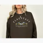 Woman wearing an espresso brown Comfort Colors t-shirt featuring the Flagstaff Arizona GPS coordinates 35.20°N 111.65°W printed at the front chest center