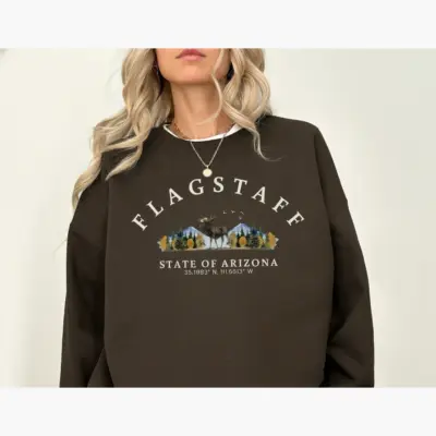 Woman wearing an espresso brown Comfort Colors t-shirt featuring the Flagstaff Arizona GPS coordinates 35.20°N 111.65°W printed at the front chest center