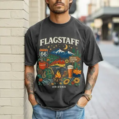 Man wearing denim blue Comfort Colors t-shirt featuring Flagstaff Coconino National Forest camp-style adventure graphic with pine trees and mountain peaks