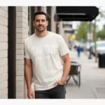 flagstaff-varsity-shirt-flg-az-hometown-pride-tee-comfort-co-urban-street-male-adult-ivory.webp Man wearing ivory Comfort Colors t-shirt with FLG AZ varsity block lettering Flagstaff Arizona hometown pride graphic on urban street