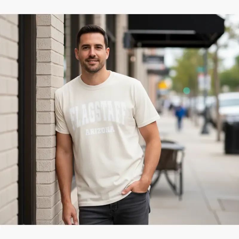flagstaff-varsity-shirt-flg-az-hometown-pride-tee-comfort-co-urban-street-male-adult-ivory.webp Man wearing ivory Comfort Colors t-shirt with FLG AZ varsity block lettering Flagstaff Arizona hometown pride graphic on urban street