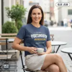 Mature woman wearing a Blue Jean Comfort Colors t-shirt featuring a Portsmouth New Hampshire lighthouse city pride graphic with the tagline History Lights Our Way