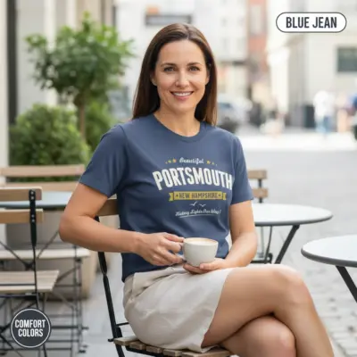 Mature woman wearing a Blue Jean Comfort Colors t-shirt featuring a Portsmouth New Hampshire lighthouse city pride graphic with the tagline History Lights Our Way