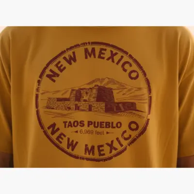 Mustard garment-dyed Comfort Colors t-shirt closeup showing Taos New Mexico souvenir graphic with mountain and adobe design detail