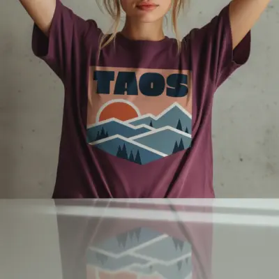 Woman wearing a berry Comfort Colors t-shirt featuring a minimalist Taos New Mexico skyline illustration with adobe architecture and Wheeler Peak