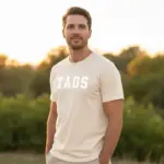 Man wearing ivory Comfort Colors t-shirt with bold varsity block lettering Taos New Mexico design outdoors in natural light